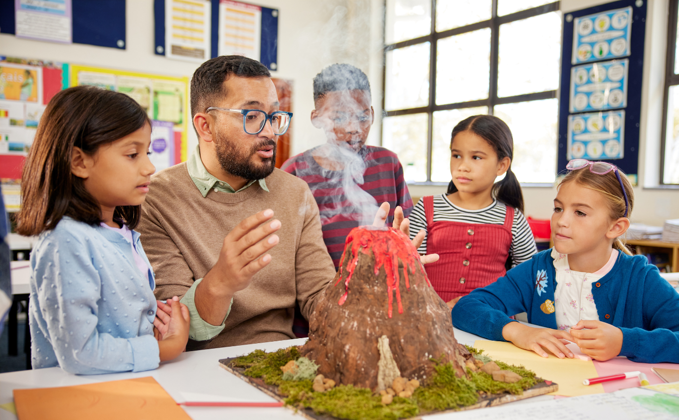 A teacher explaining a model volcano to three young students